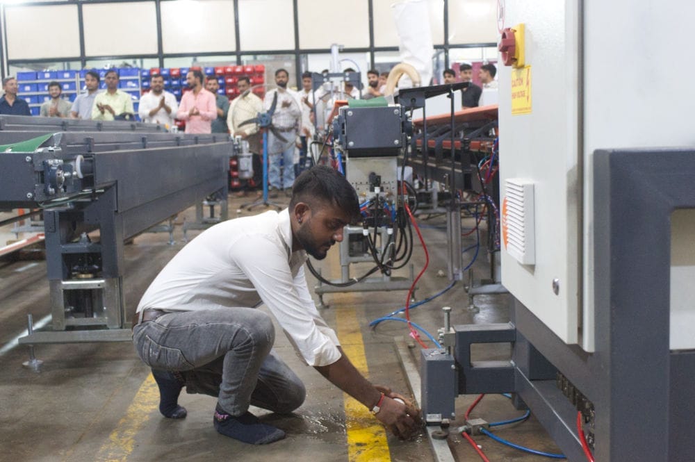 Worker adjusting machinery parts in busy factory.