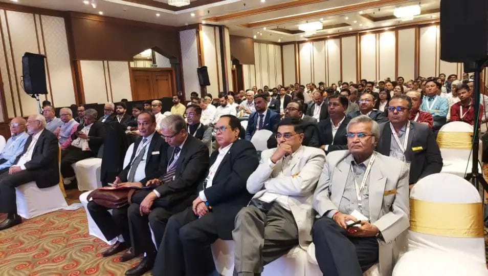 Business conference attendees seated in large room.