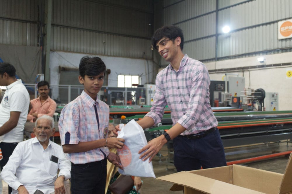 Man handing gift to boy in factory setting.