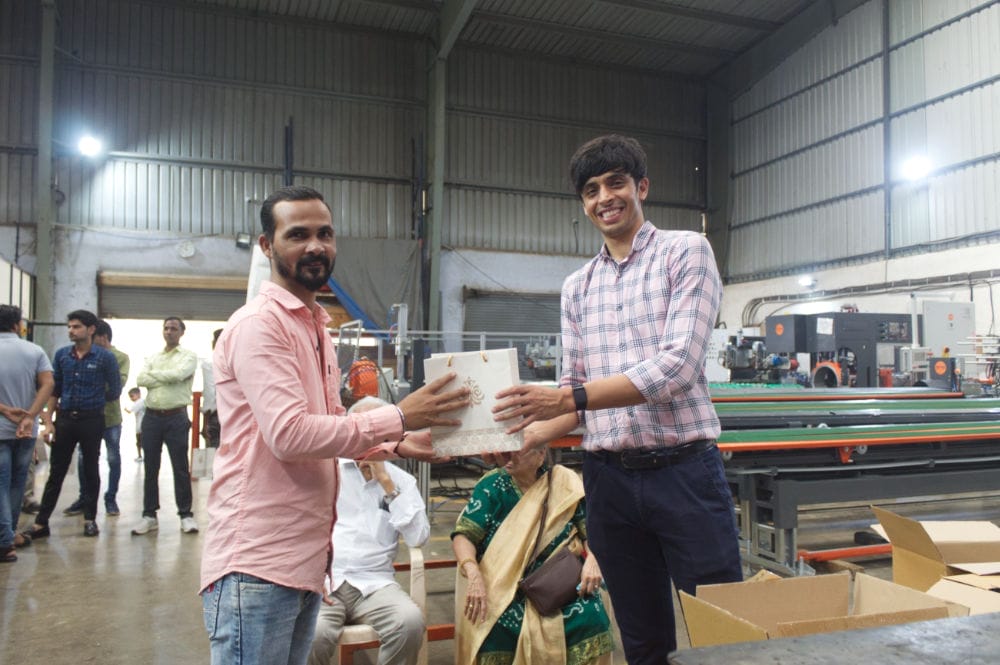 Two men exchanging gift in factory setting.