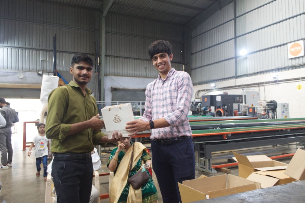 Two men exchanging gift in factory setting.