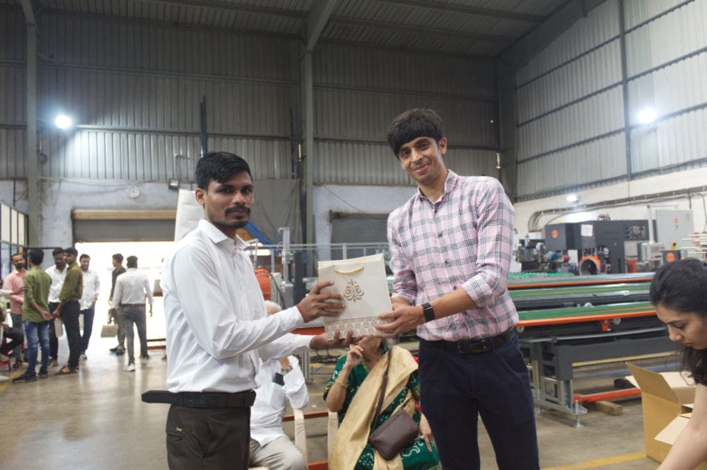 Two men exchanging gifts in a factory setting.
