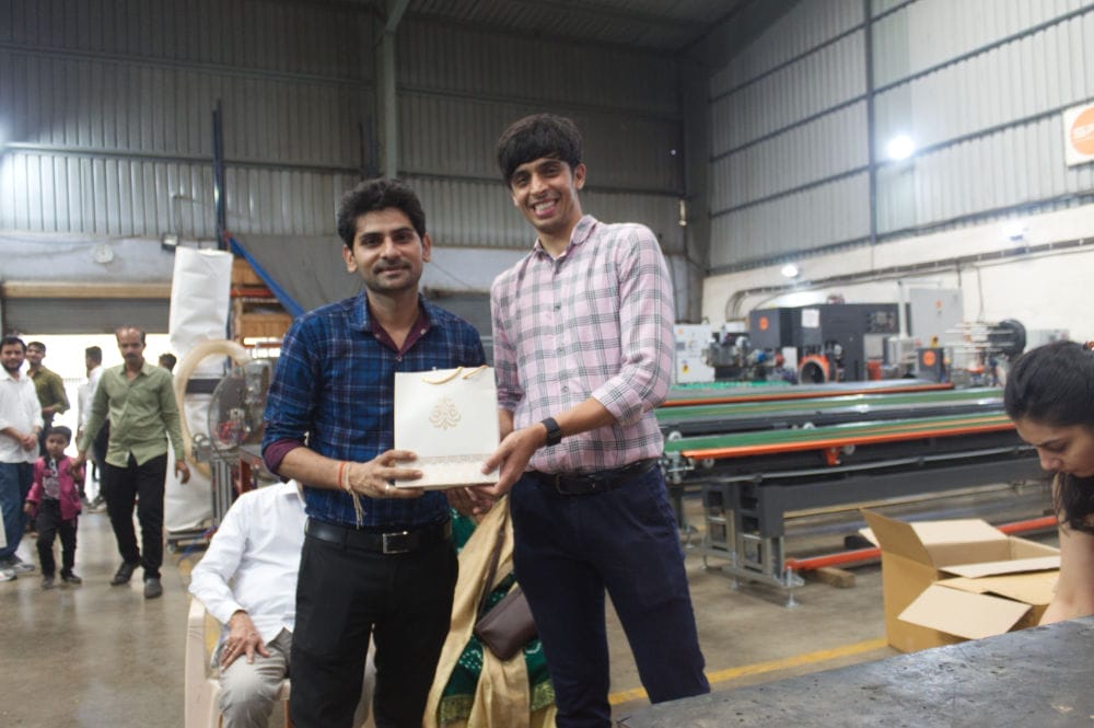 Two men smiling in a factory, holding a gift.
