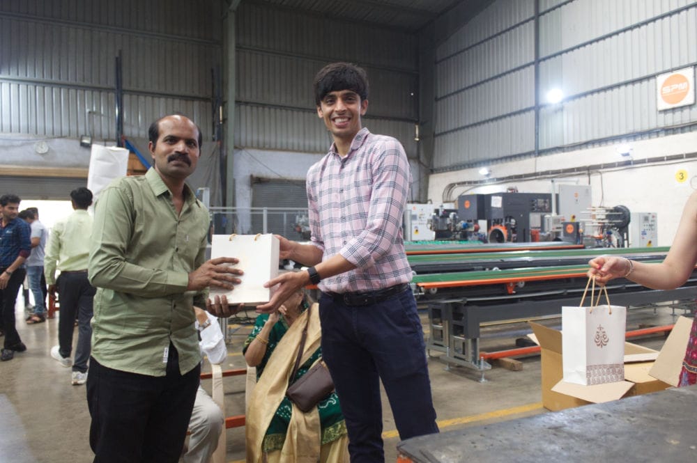 Two men exchanging gift bags in factory setting.
