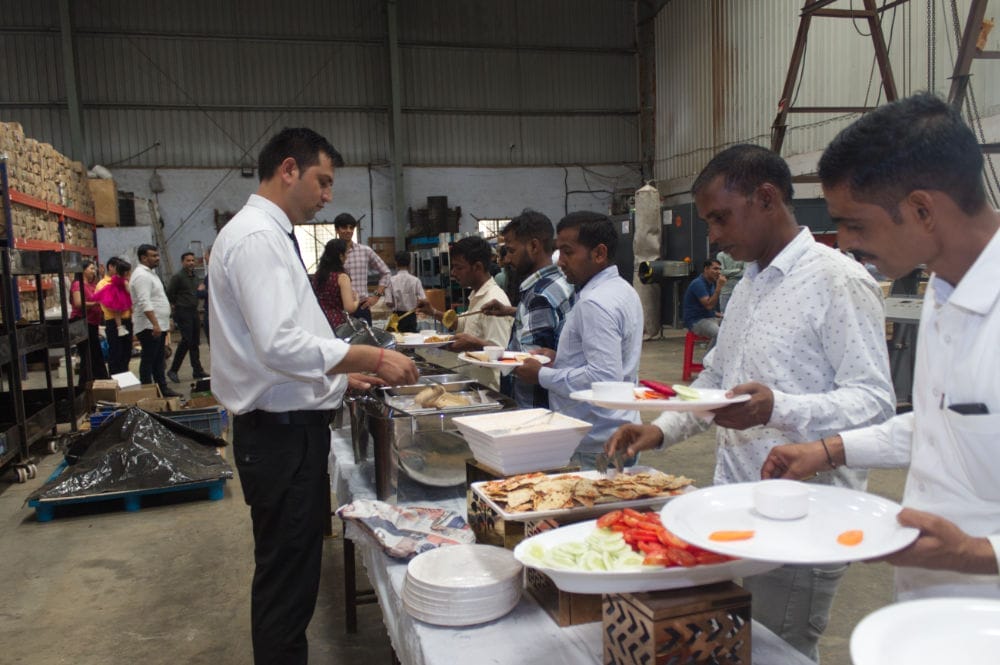 People serving food at buffet in industrial setting.