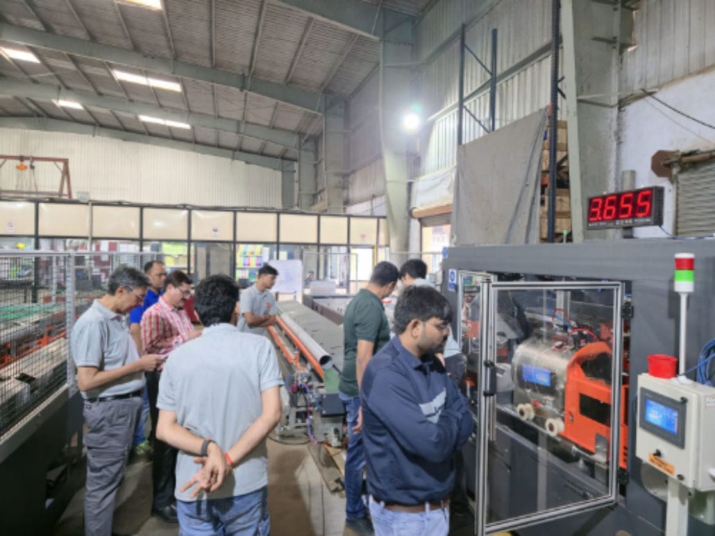 People working in a factory setting, industrial machinery present.